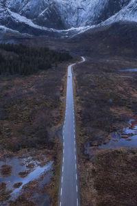 Drone view of long narrow asphalt roadway with making lines running between wetland with withered grass in nature of norway