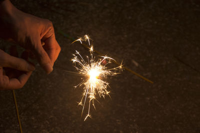 Cropped hand holding sparkler at night