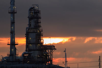 Cranes in factory against sky during sunset