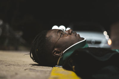 Close-up of thoughtful young man lying down on sidewalk at night