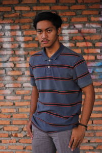 Portrait of young man standing against brick wall