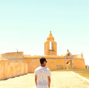 Rear view of man standing outside temple against clear sky