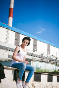 Young woman sitting on barricade against factory