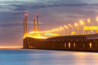 Illuminated bridge over sea against sky at night