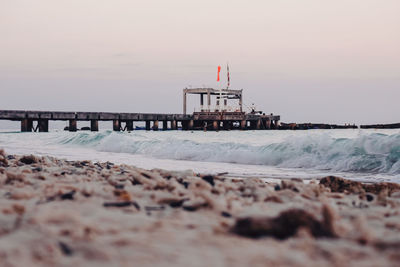 Pier on beach against sky during sunset