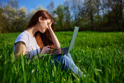 Young woman using laptop while sitting on grassy field