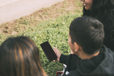 View from the back group of laughing latinos sitting on the ground in a park with a smartphone