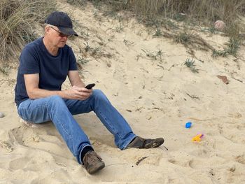 Man sitting on a sandy beach while doing remote work on his smartphone
