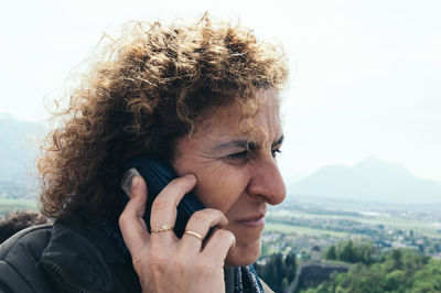 Mature woman talking on phone at mountain against sky