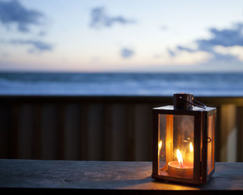 Close-up of lit candle on table at beach during sunset