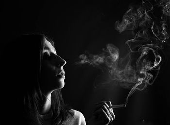 Close-up of woman smoking cigarette over black background