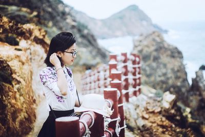 Side view of young woman standing by railing on mountain
