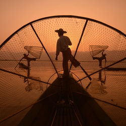 Fishermen on boats in lake against sky during sunset