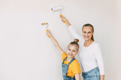 Beautiful and happy mom and daughter paint the walls in the apartment white.