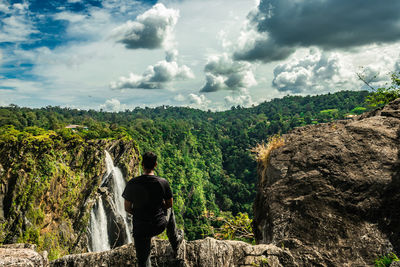 Rear view of man looking at waterfall against sky