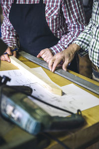 Midsection of man and woman measuring wood in workshop