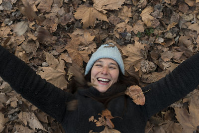 High angle view of smiling woman lying on autumn leaves