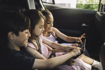 Male and female siblings using tablet pc while traveling in car