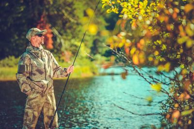 Mid adult man fishing while standing at lakeshore in forest