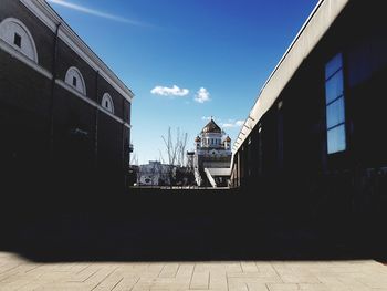 Empty footpath amidst buildings against sky on sunny day