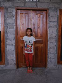 Full length of girl standing against old wooden door
