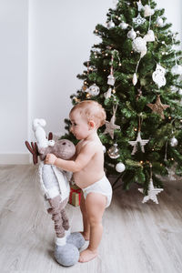 Cute baby girl wearing diaper decorating christmas tree