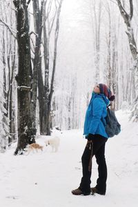 Woman with dog looking up while standing in forest during winter