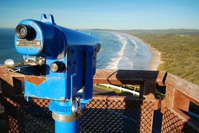 Close-up of coin-operated binoculars by sea against blue sky