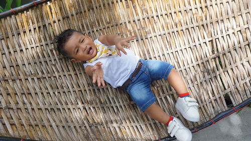 High angle view of crying boy lying on wicker bed