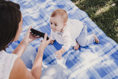 High angle view of woman showing mobile phone to baby girl at park