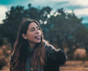 Woman sticking out tongue against trees