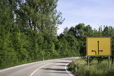 Road sign by trees against sky