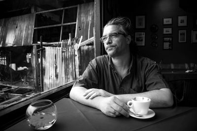 Man looking away while sitting with coffee cup on table at cafe