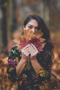 Portrait of woman holding maple leaf during autumn