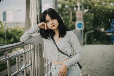 Young woman looking away while standing against railing