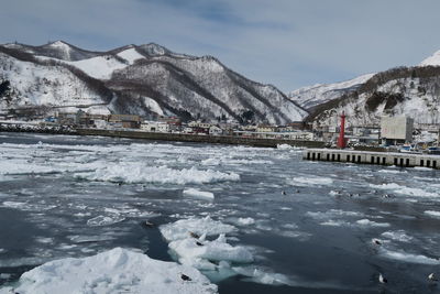 Frozen lake by snowcapped mountain against sky