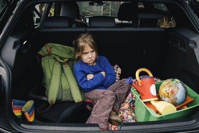 Angry girl with arms crossed sitting in electric car trunk