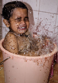 Close-up of playful boy splashing water while sitting in bucket at bathroom