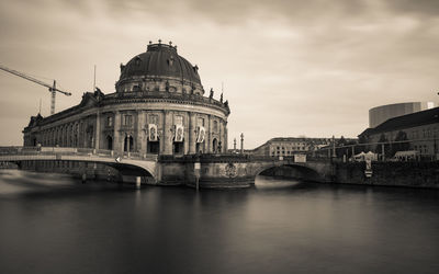 Bridge over river by buildings against sky in city