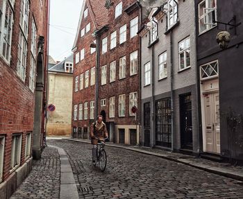 Rear view of person riding bicycle on street amidst buildings