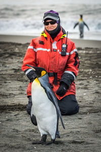 Woman kneeling while looking at penguin on sand