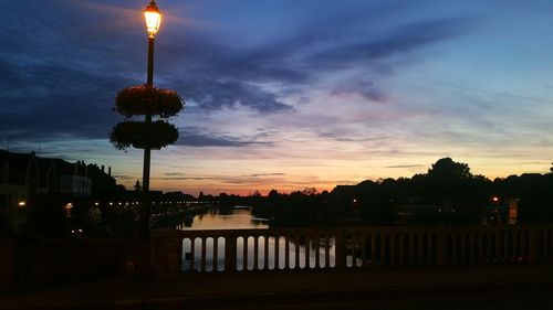 Illuminated city by river against sky