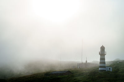 Lighthouse on landscape against sky during foggy weather