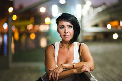 Portrait of smiling young woman standing against illuminated city at night