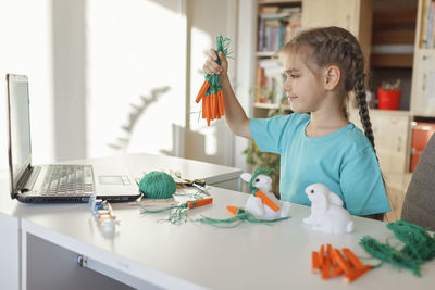 Cute girl doing craft while watching videos on laptop at home