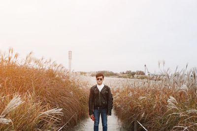 Portrait of young man standing on field against sky