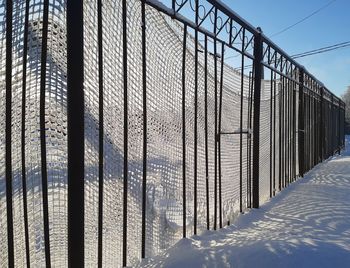 Snow covered metal fence against sky