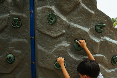 Rear view of boy playing on climbing wall at playground