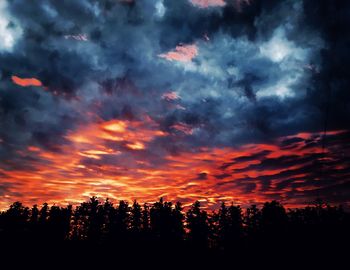 Silhouette trees against dramatic sky during sunset