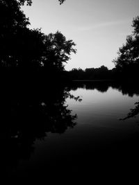 Silhouette trees by lake in forest against sky